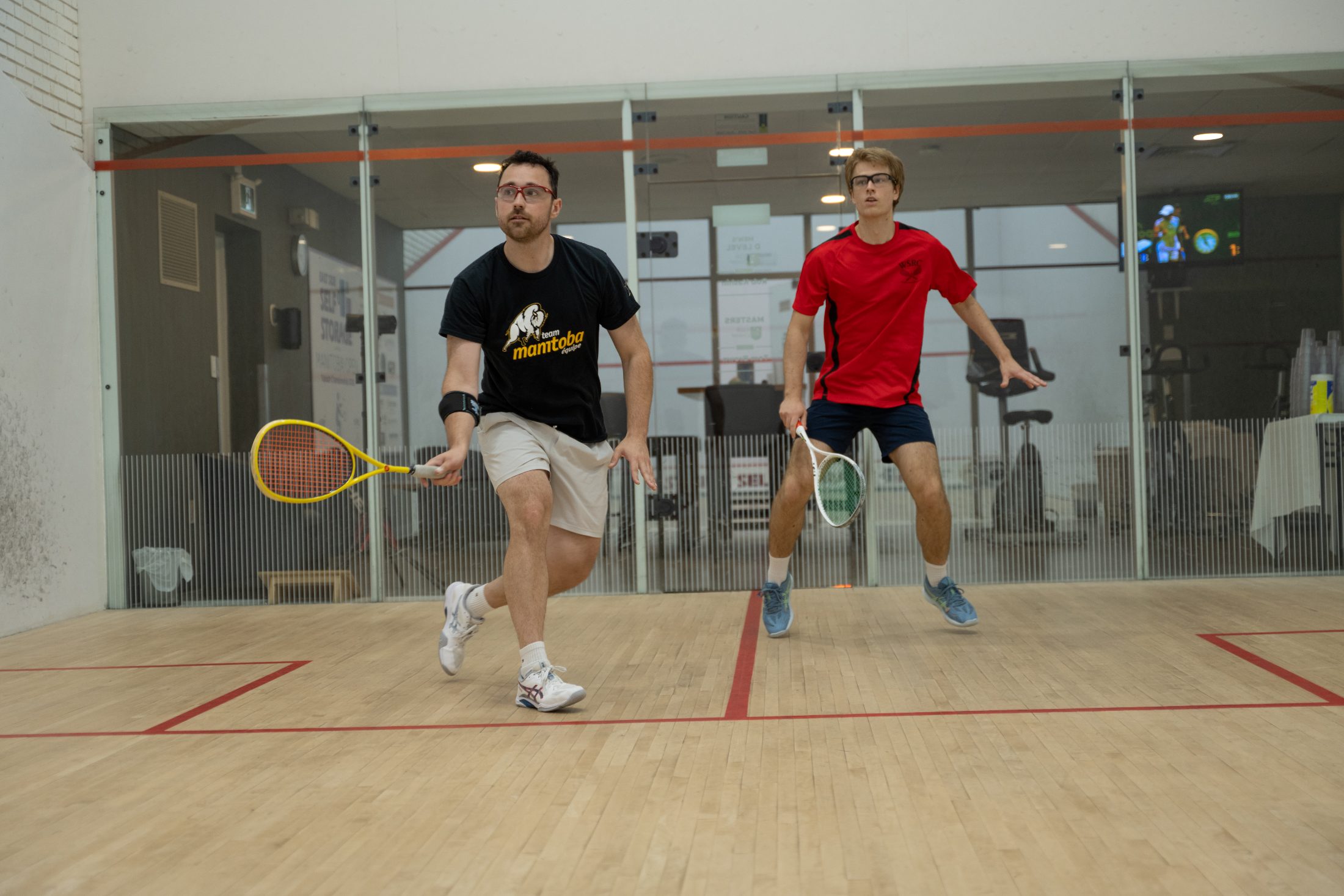 A rally in front of the show court glass at the Winnipeg Squash Racquet Club